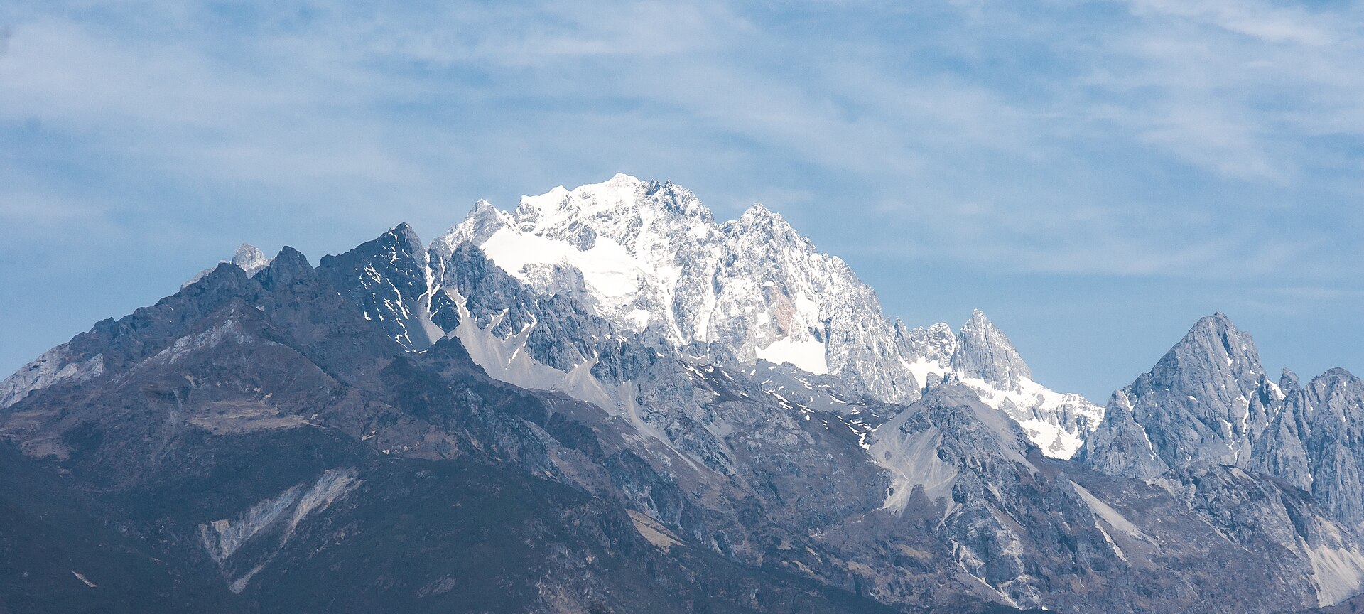 玉龙雪山的群峰：主峰覆雪，岩石棱线分明，湛蓝天空下云絮轻拂