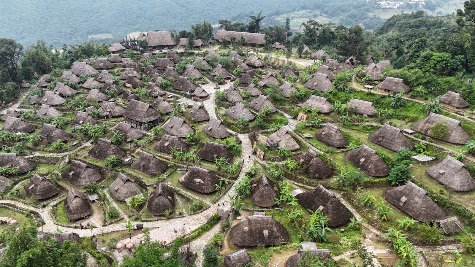 翁丁佤寨航拍：茅草顶的佤族木楼错落铺在绿坡上，四周群山环抱